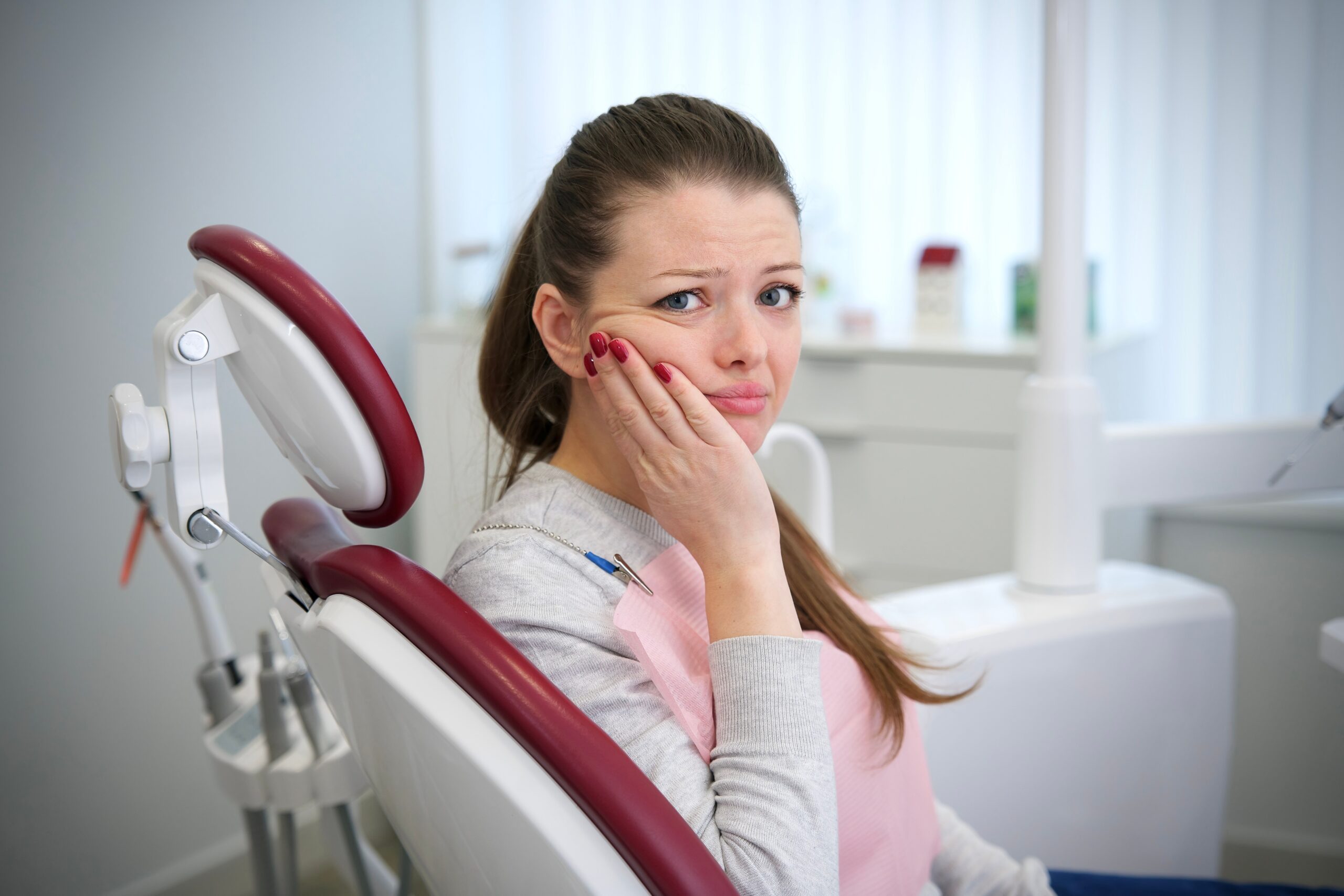 Sad, frustrated young woman is crying, holding cheek, suffering from serious teeth pain, possible dental emergency