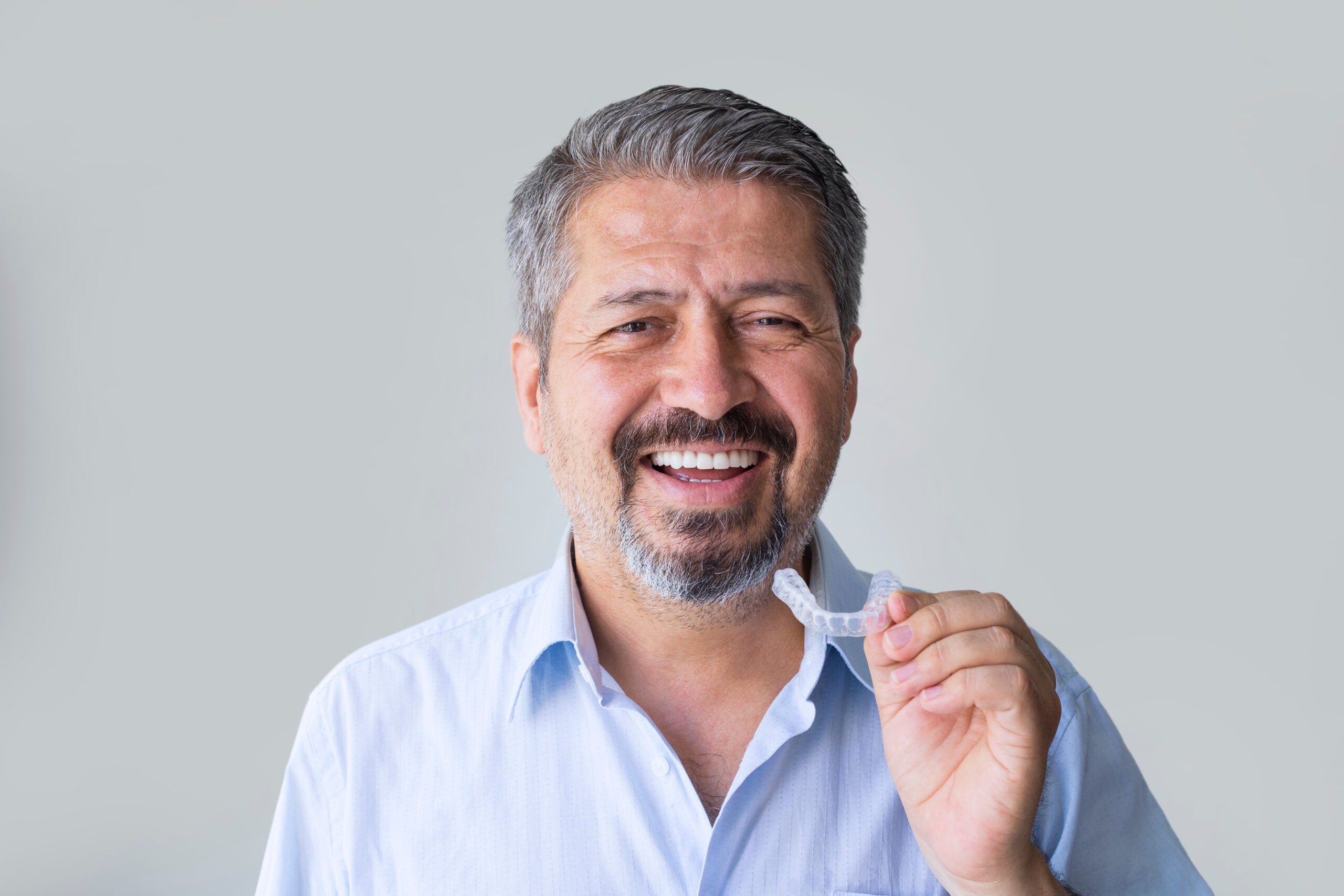 adult man smiling and holding his clear aligners