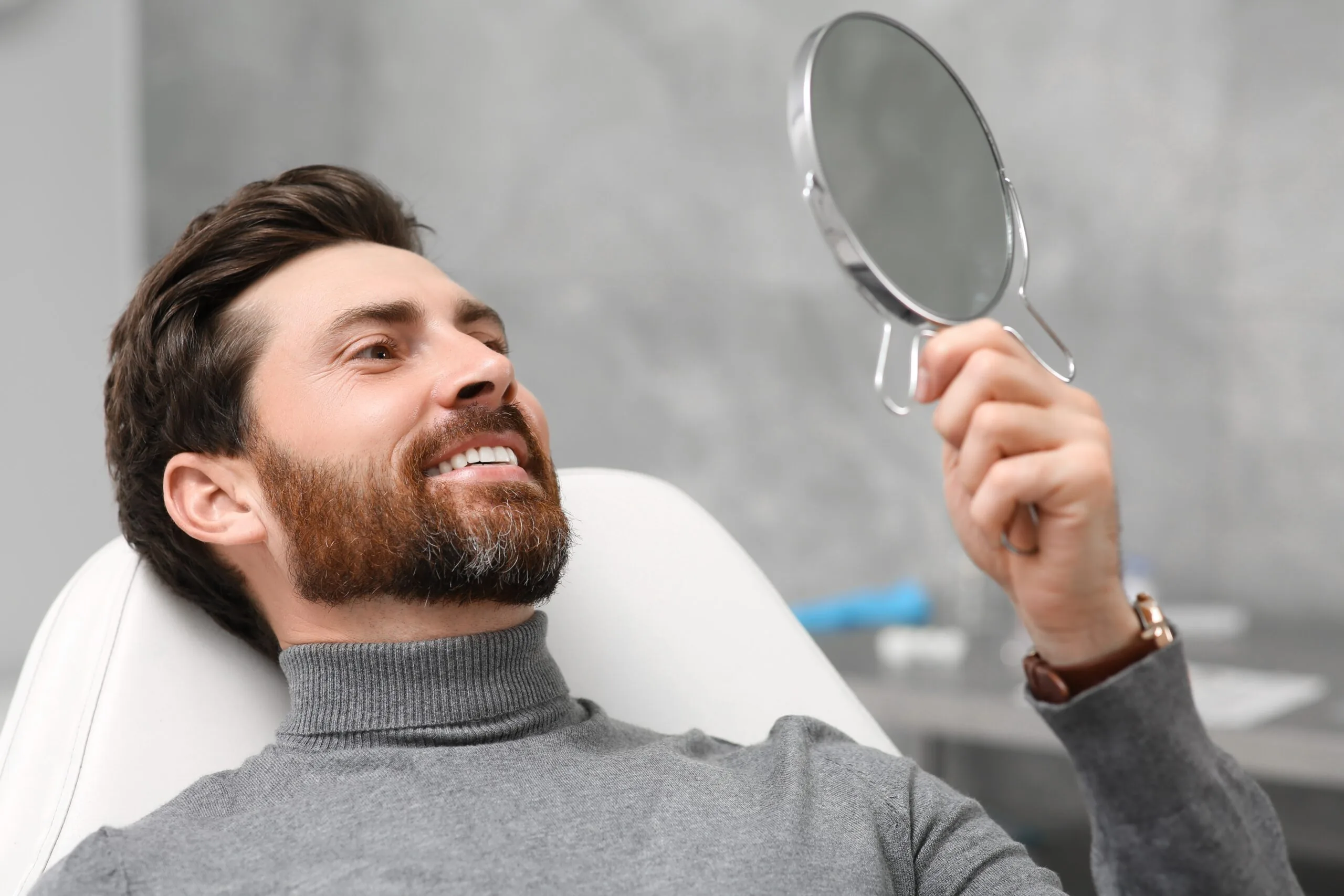 man smiling in mirror, looking at new dental implants in office